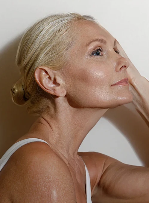 A close up shot of the side of a women's face looking to the right of the image. She has light eyes and blonde hair and her hand Is touching the opposite side of her face. - Facelift in Los Angeles, CA