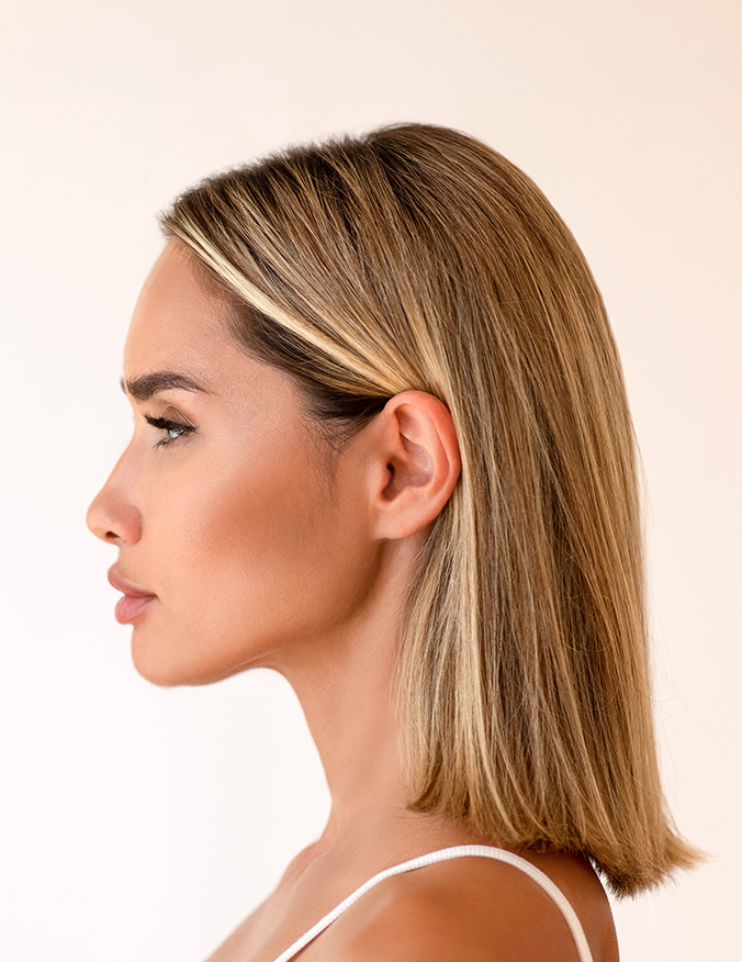 A clean profile shot of a woman with blonde, shoulder-length hair. She is looking straight ahead, showcasing a straight nasal bridge and a well-defined jawline against a plain, off-white background. - Nasal reconstruction in Los Angeles, CA