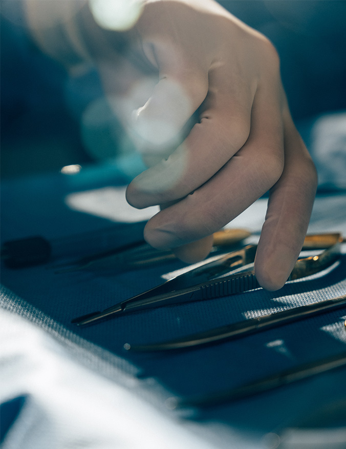 A close-up, high-angle shot focusing on a surgeon’s gloved hand reaching for stainless steel medical instruments laid out on a blue sterile surgical tray. The lighting is bright and clinical, emphasizing the precision of the surgical tools. - Septoplasty in Los Angeles, CA